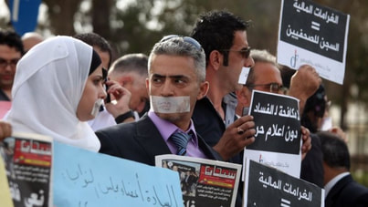 Photograph of protesters with tape over their mouths holding signs written in Arabic